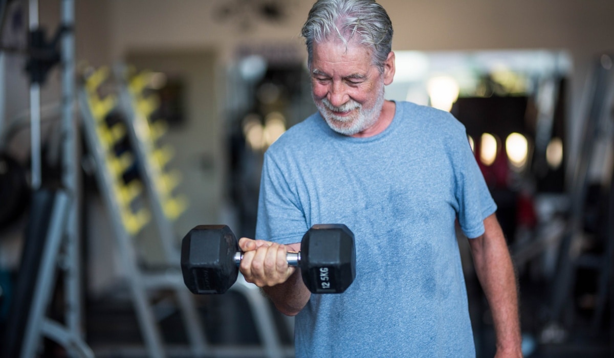 Elderly man strength training with dumbbell in gym while focusing on muscle growth and creatine benefits